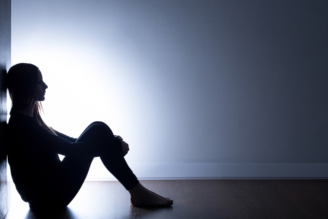 a teenage girl sitting on the floor alone in a dark room