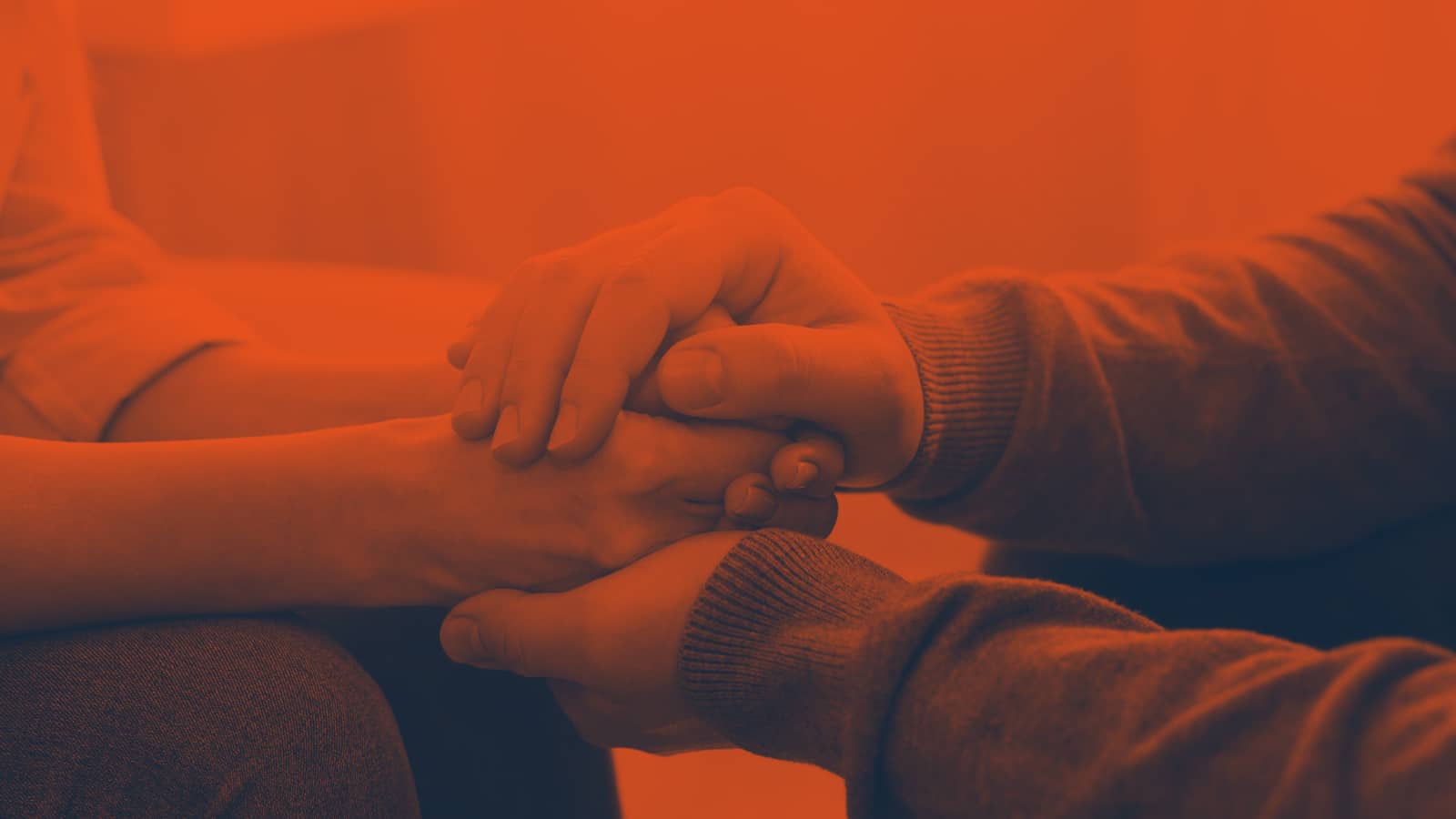 Two people sitting down with a reassuring holding of hands