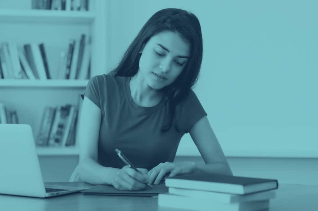 A young woman writing in a notepad at a desk