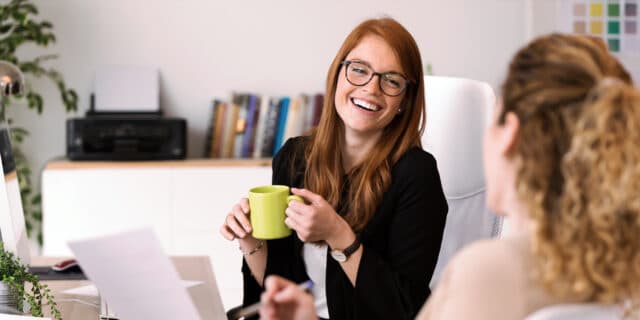An image of two women in an office environment, talking to one another and smiling