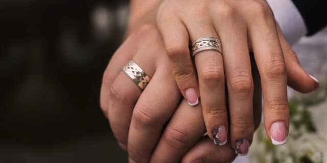An image of a woman's hand wrapped around one another, with colourful nails and rings on her hand