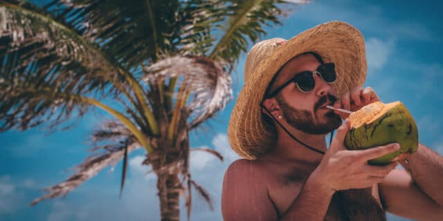 An image of a man drinking from a coconut under a palm tree