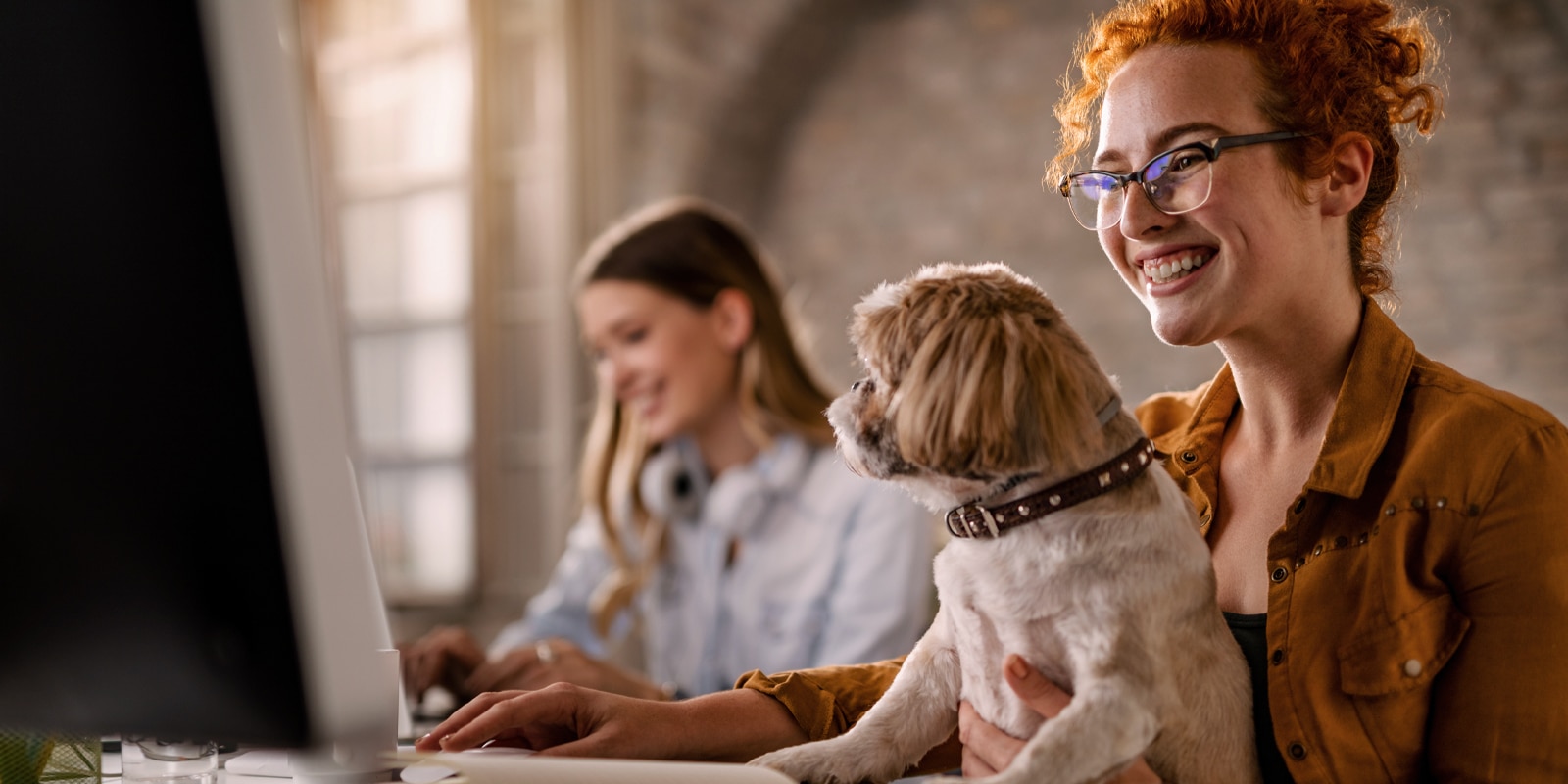 An image of 2 people and a dog, smiling and working on their computers