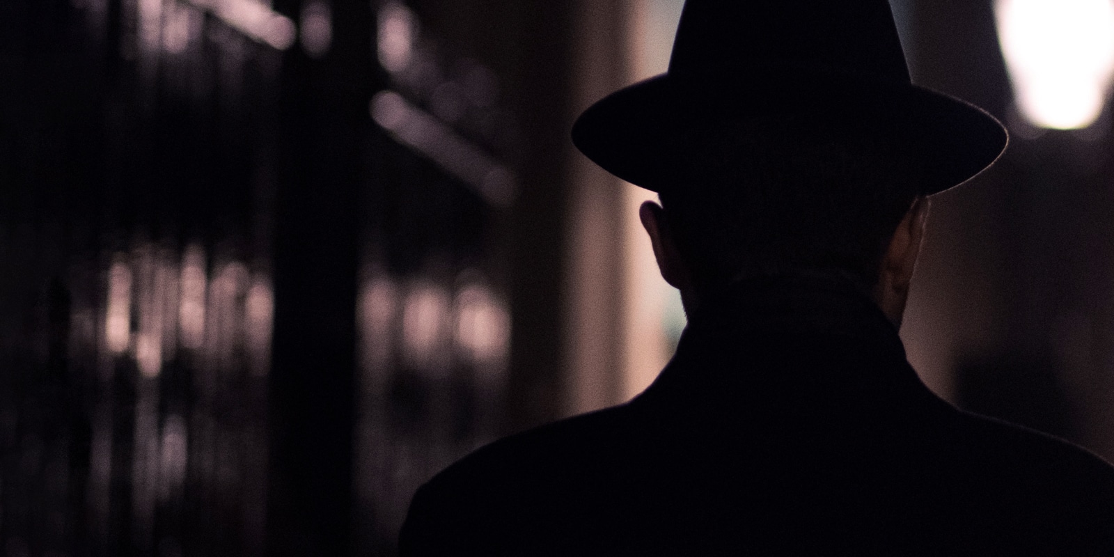 An image of a man in the dark with a fedora hat on