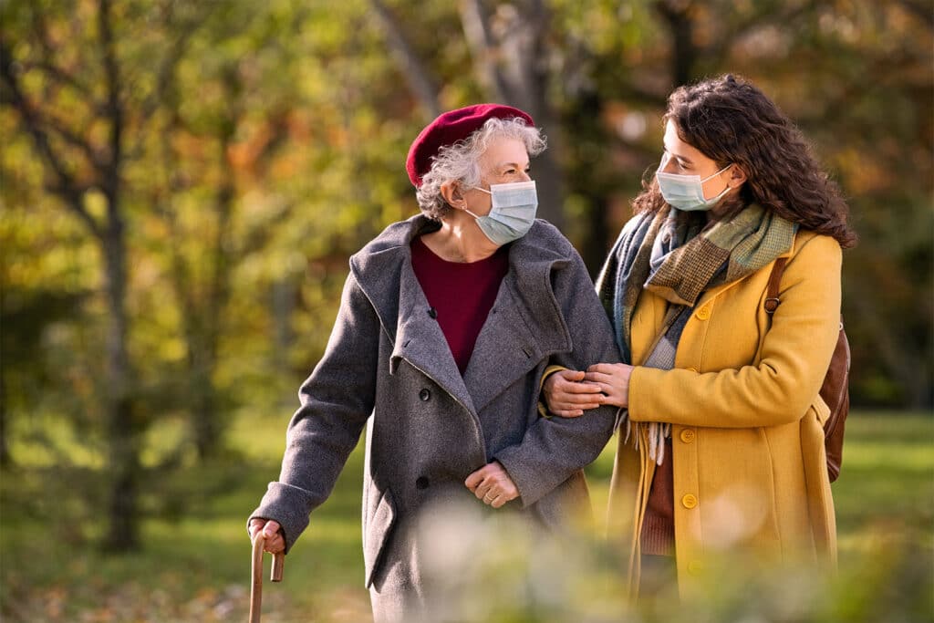 Woman walking in park with elderly woman, both dressed for winter
