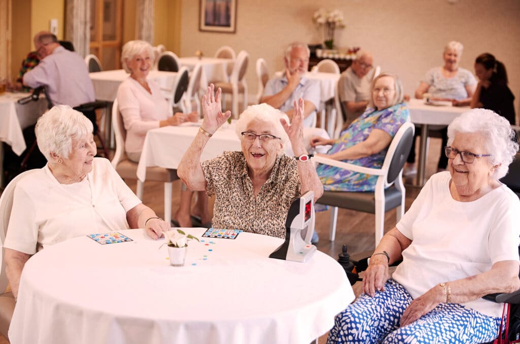 Elderly people in care home seated at a table laughing