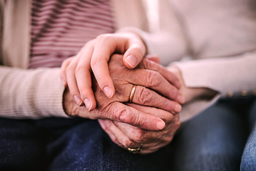 Elderly person and younger woman clasping hands