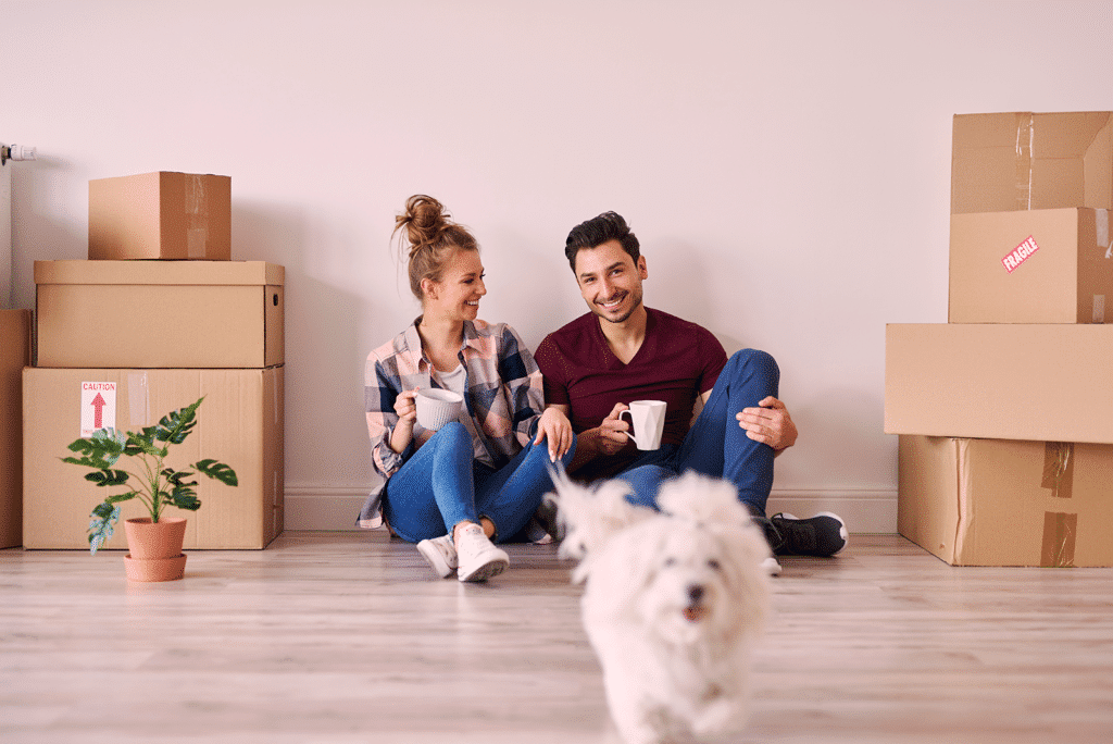 Young couple in living room with boxes and a white dog