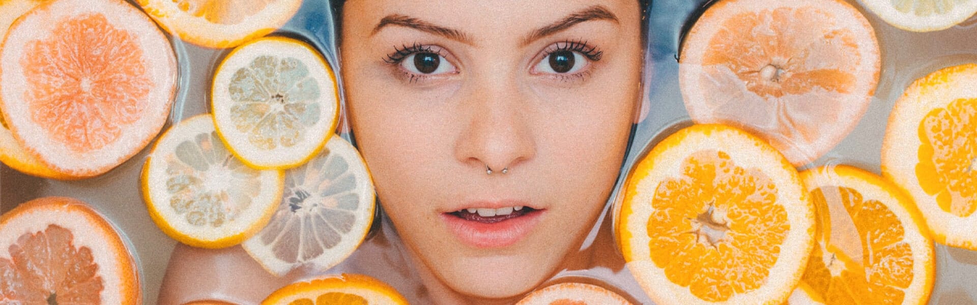 a young woman lies in a bath of orange and yellow citrus fruit slices