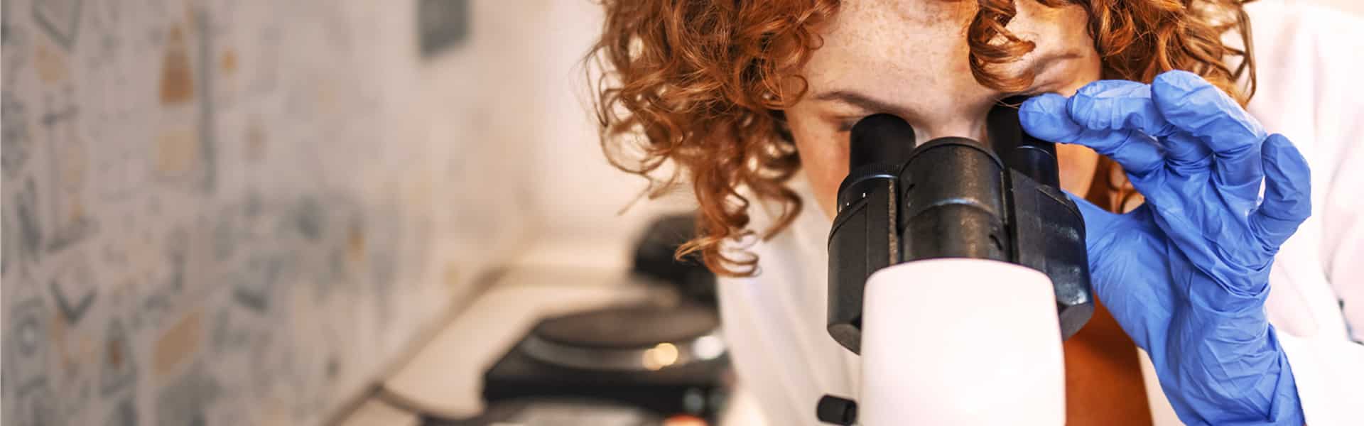 A young woman with red hair studies using a microscope