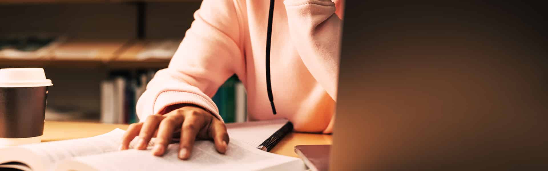 a young woman wearing a pink hoodie working on her laptop