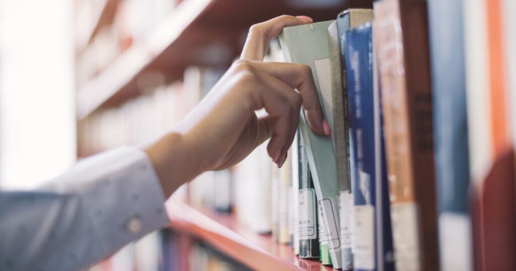 a person reaching for a book on a shelf in a library
