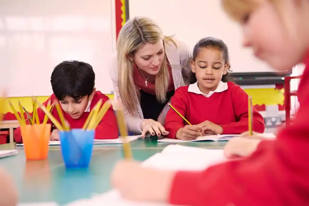 Teaching Assistant helps pupil with her work in the classroom.