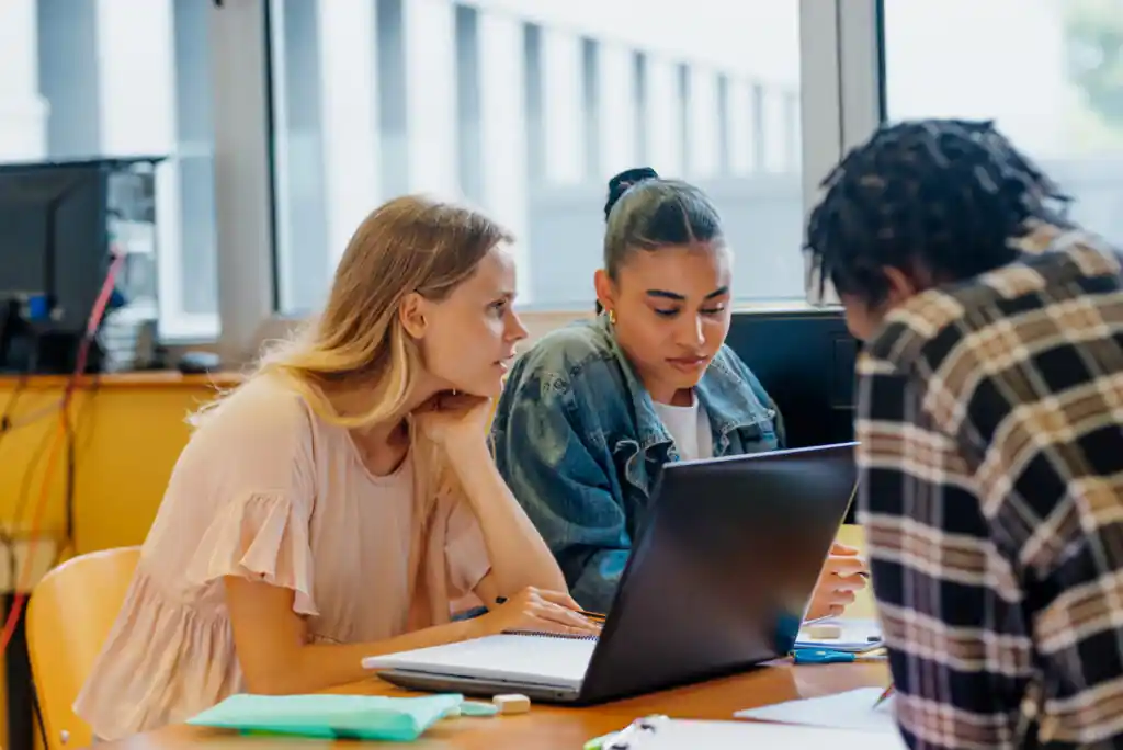 University students working in a group on a laptop with their classmates sitting at a table.